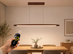 UNIKAA modern linear wooden pendant light for kitchen island being controlled with remote in a modern dining room setup.