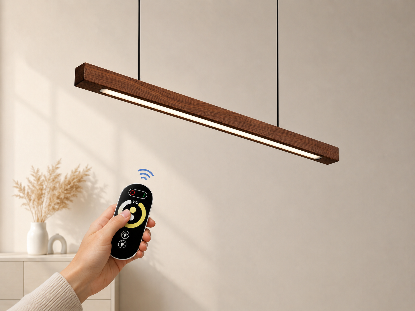 Hand holding a remote control next to a modern pendant light fixture.